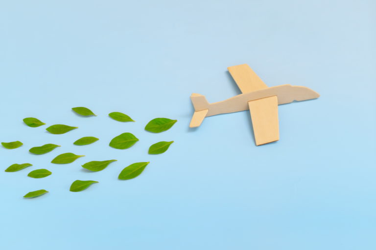 Wooden airplane model emitting fresh green leaves on blue background. Sustainable travel; clean and green energy; and biofuel for aviation industry concept.