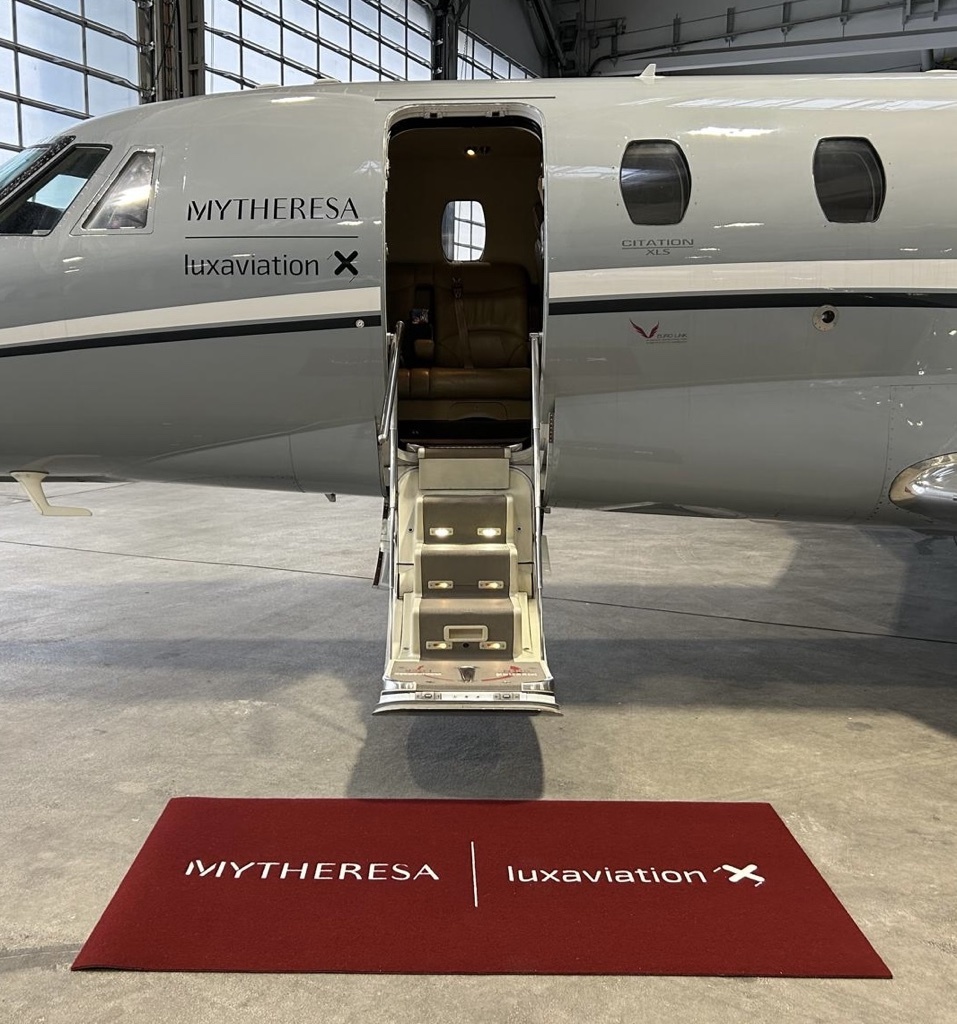 Privatjet von Luxaviation mit Mytheresa-Co-Branding, geöffneter Kabinentür und rotem Empfangsteppich in einem Hangar.